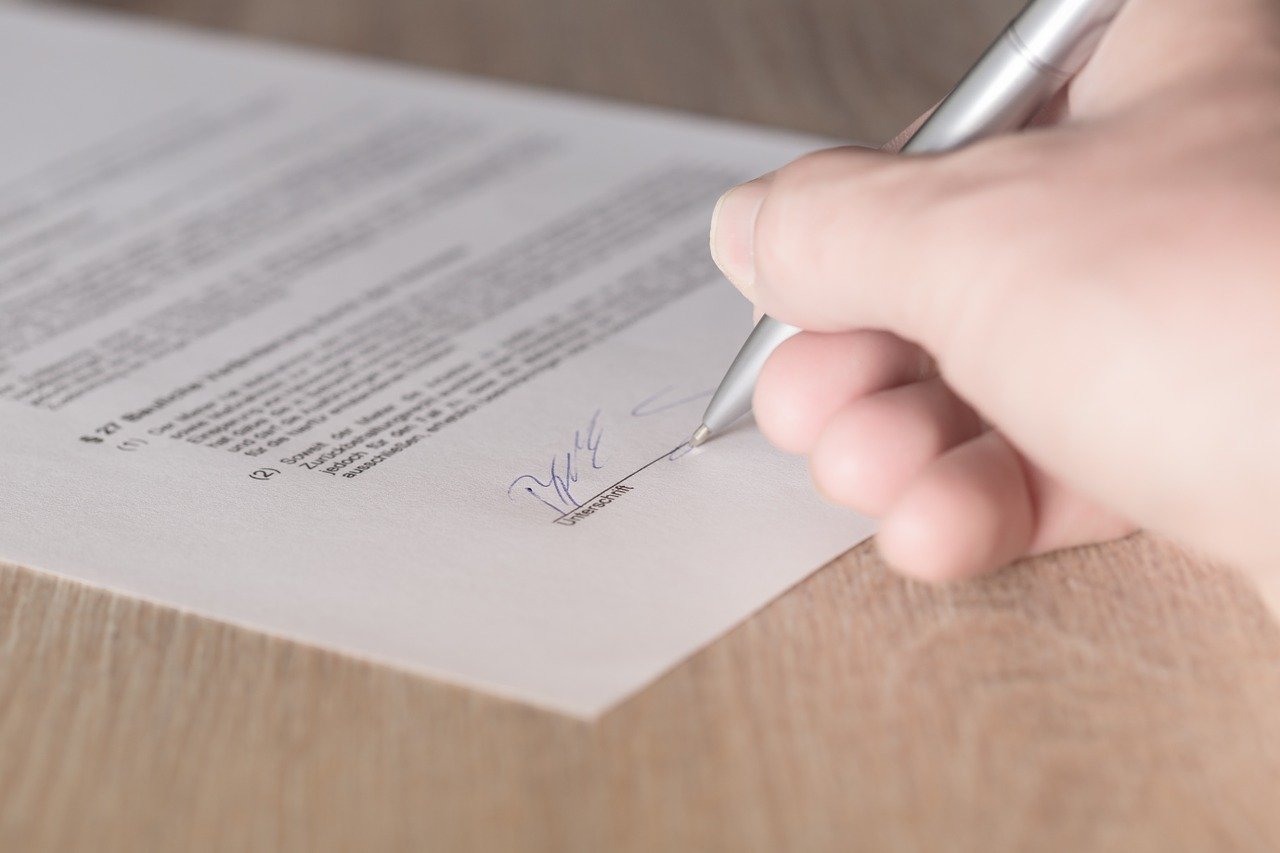Eine Hand unterschreibt einen Mietvertrag mit Kugelschreiber auf der Unterschriftszeile